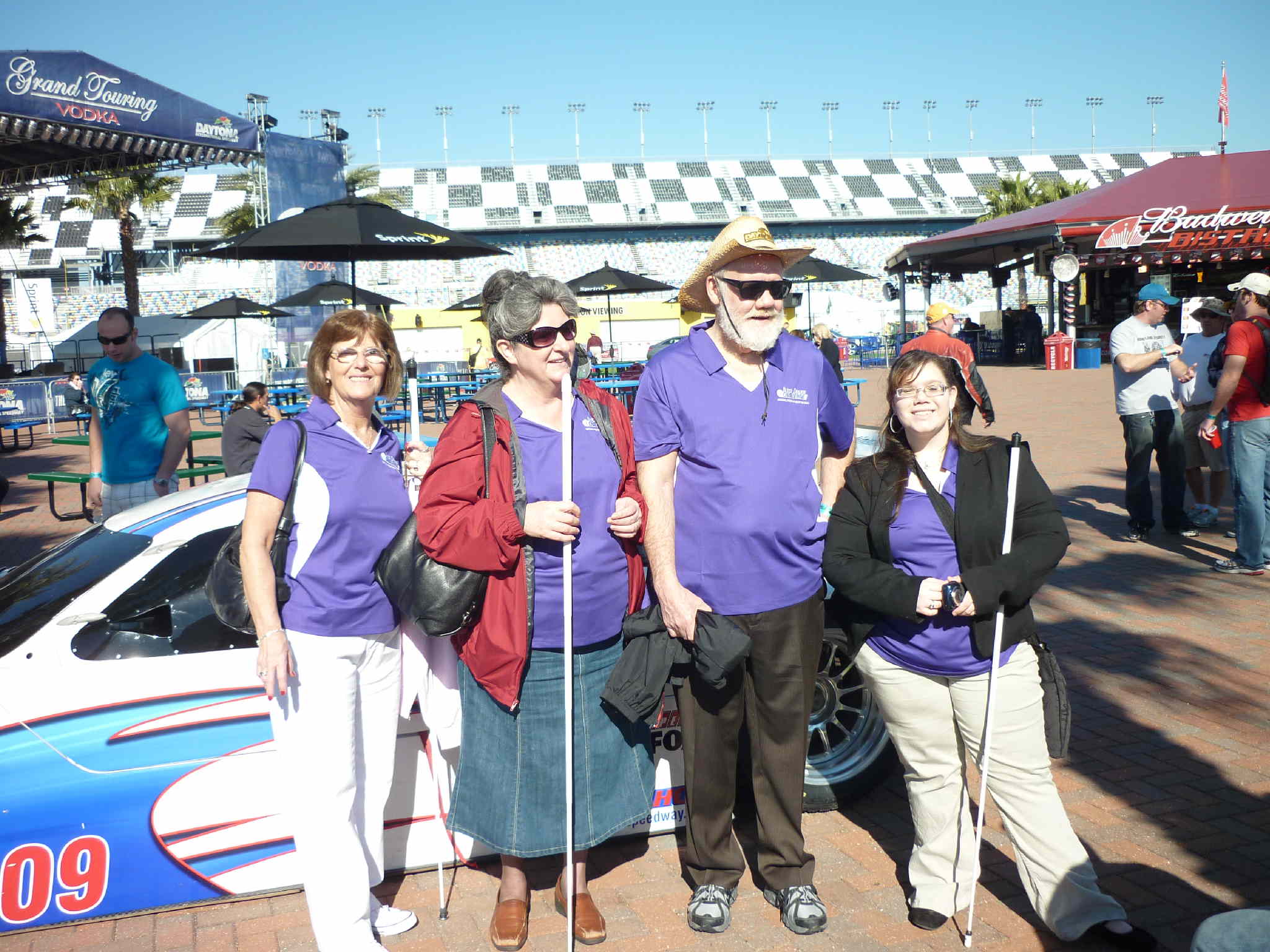 Pamela and John Glisson, Angela Dehart and Cathy Jackson standing in front of a race car at the race track